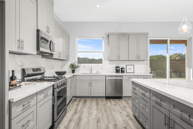 kitchen with gray cabinetry, hanging light fixtures, tasteful backsplash, light stone counters, and appliances with stainless steel finishes