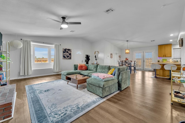 living room featuring ceiling fan, wood finished floors, visible vents, baseboards, and vaulted ceiling