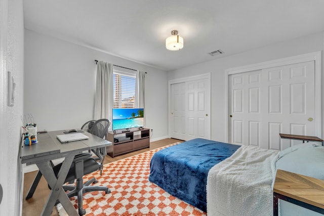 bedroom with baseboards, visible vents, light wood-style flooring, and two closets