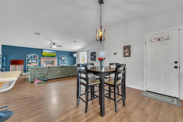 dining space featuring a fireplace, visible vents, ceiling fan, vaulted ceiling, and wood finished floors