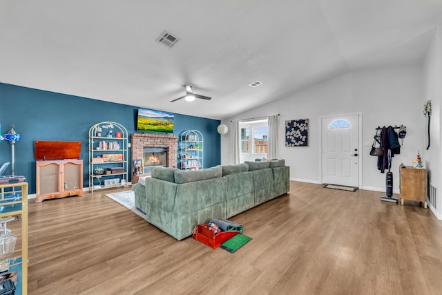 living area with ceiling fan, lofted ceiling, wood finished floors, visible vents, and a brick fireplace