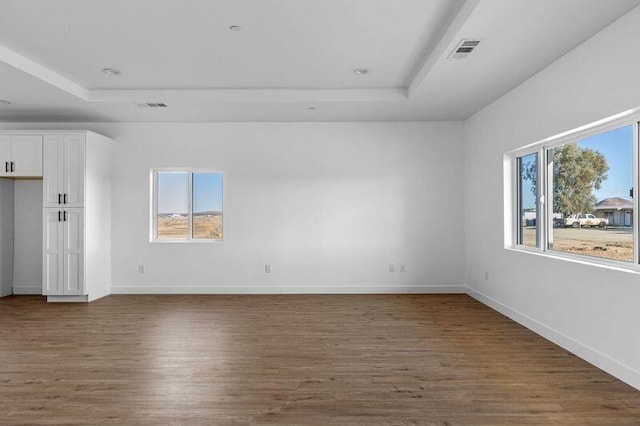 spare room with a tray ceiling, dark wood-style floors, visible vents, and baseboards