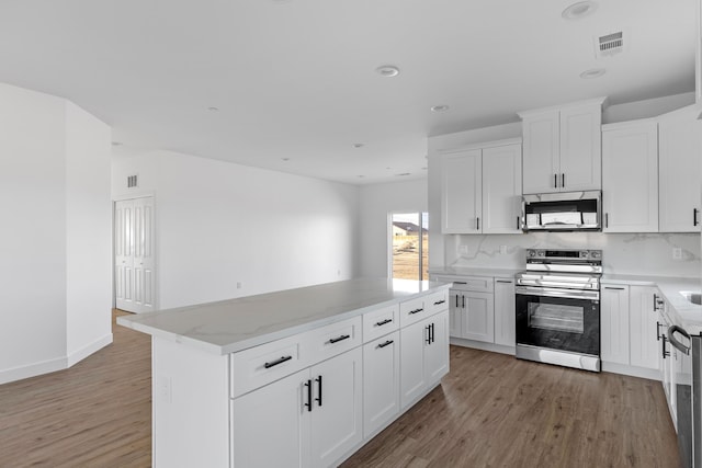 kitchen with light stone counters, appliances with stainless steel finishes, a center island, and light wood-style floors