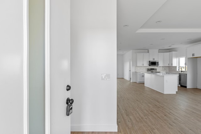 kitchen featuring tasteful backsplash, light wood-type flooring, light countertops, stainless steel appliances, and white cabinetry