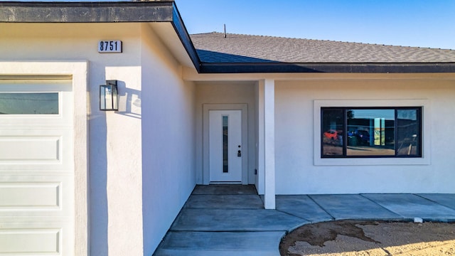 doorway to property featuring a garage, roof with shingles, and stucco siding