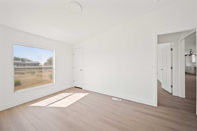 unfurnished room with an inviting chandelier and light hardwood / wood-style flooring