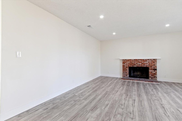 unfurnished living room with light wood-type flooring, a textured ceiling, and a brick fireplace