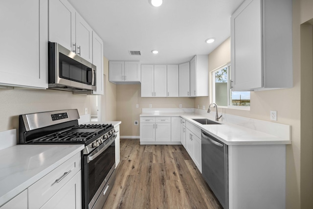 kitchen with appliances with stainless steel finishes, visible vents, a sink, white cabinetry, and light wood-type flooring