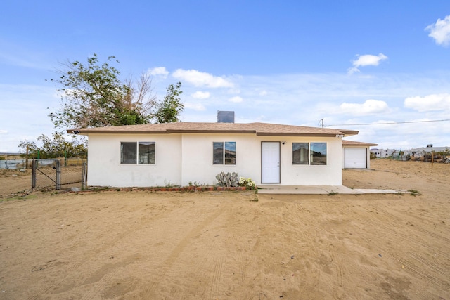 rear view of house with stucco siding, a gate, fence, and a garage