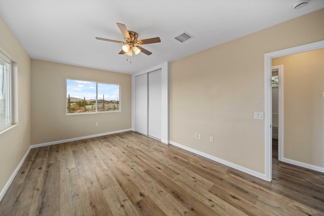 unfurnished bedroom featuring a ceiling fan, visible vents, wood finished floors, and baseboards