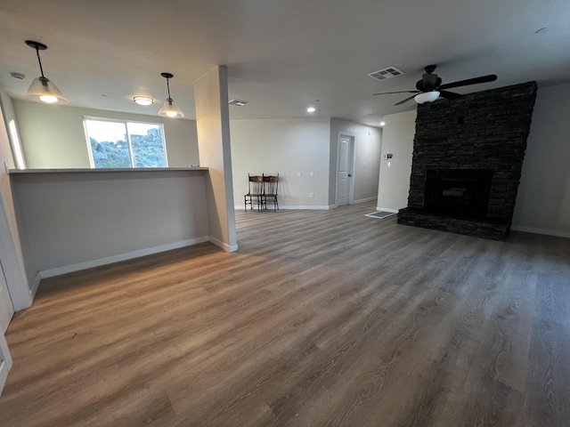 unfurnished living room featuring a stone fireplace, ceiling fan, and hardwood / wood-style flooring