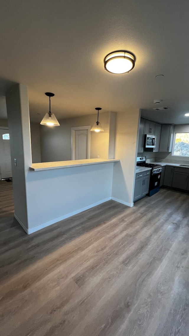 kitchen featuring pendant lighting, gas stove, gray cabinetry, and hardwood / wood-style floors