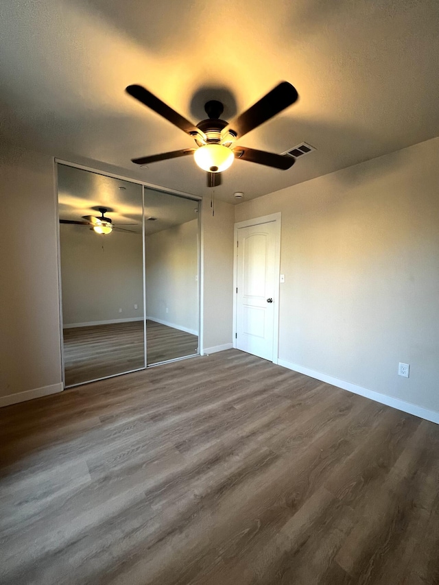 unfurnished bedroom featuring ceiling fan, wood-type flooring, and a closet