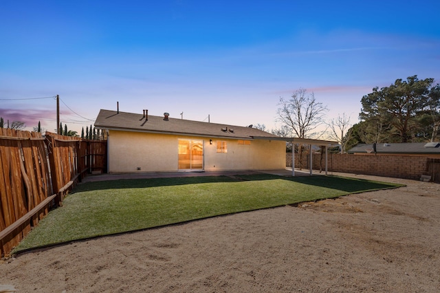 back house at dusk featuring a lawn and a patio area