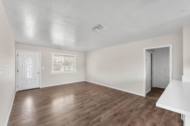 unfurnished living room with a textured ceiling and dark hardwood / wood-style flooring