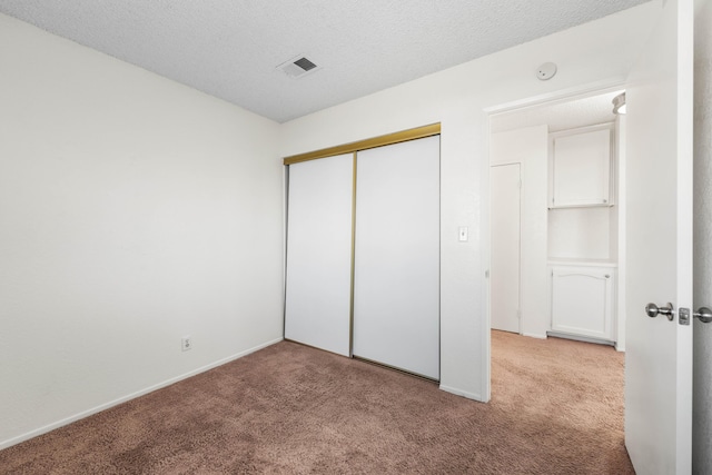 unfurnished bedroom featuring a textured ceiling, light carpet, and a closet