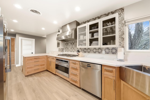 kitchen with visible vents, a peninsula, light brown cabinetry, appliances with stainless steel finishes, and wall chimney exhaust hood