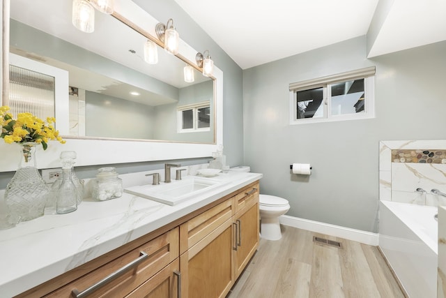 bathroom featuring visible vents, toilet, wood finished floors, a bath, and vanity