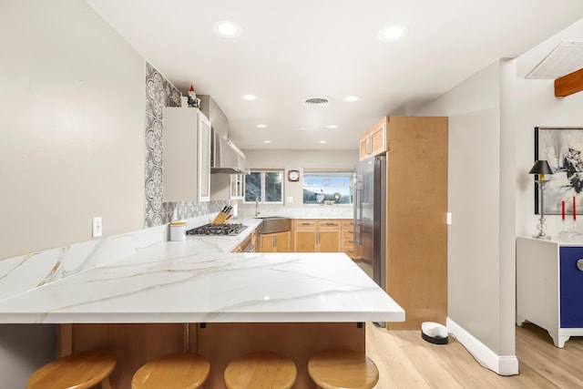 kitchen with visible vents, light brown cabinetry, a sink, light stone counters, and a peninsula