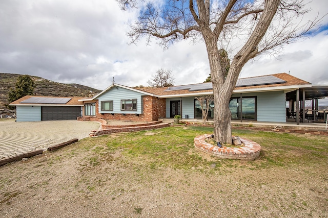 single story home with a garage, roof mounted solar panels, brick siding, and a front yard