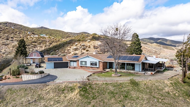 single story home featuring aphalt driveway, roof mounted solar panels, a mountain view, and a sunroom