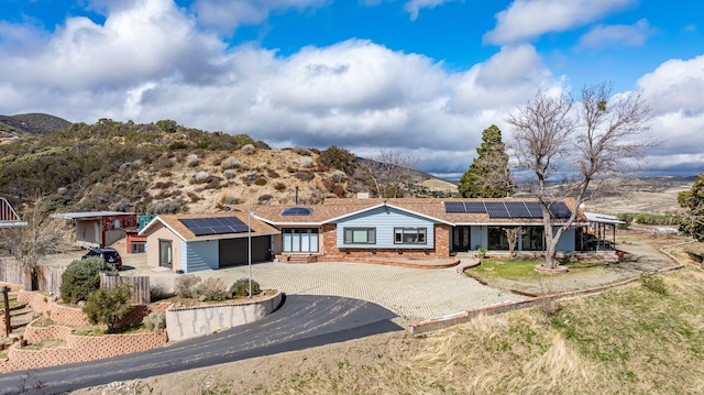 ranch-style home with roof mounted solar panels, curved driveway, fence, an attached garage, and brick siding