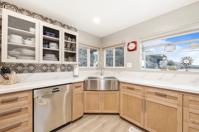 kitchen featuring glass insert cabinets, light stone countertops, light brown cabinetry, dishwasher, and a sink