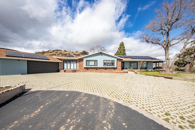 ranch-style house featuring brick siding, solar panels, driveway, and a garage