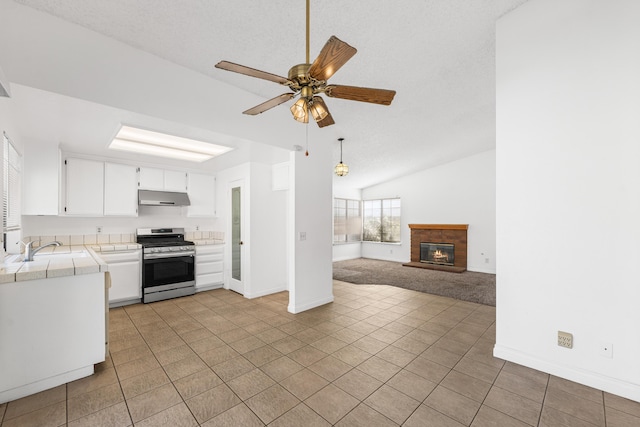 37756 E 45th St, Palmdale, CA 93552 - kitchen with stainless steel gas stove, tile countertops, under cabinet range hood, ceiling fan, and a glass covered fireplace