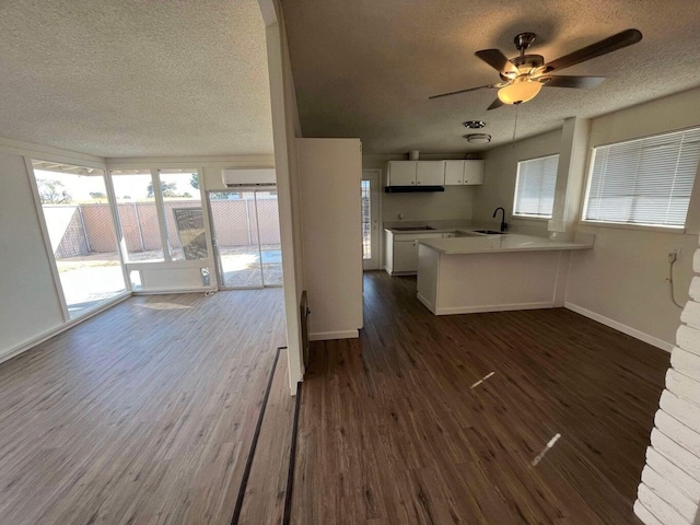 kitchen featuring sink, dark hardwood / wood-style floors, a wall mounted air conditioner, white cabinets, and kitchen peninsula