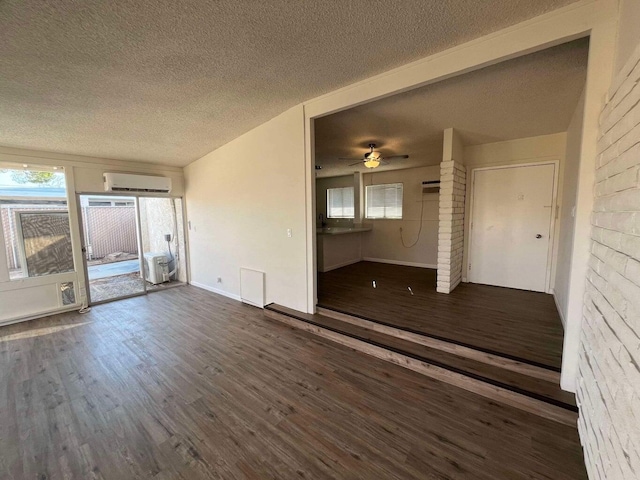 spare room featuring a wall mounted air conditioner, a textured ceiling, dark hardwood / wood-style floors, and a healthy amount of sunlight