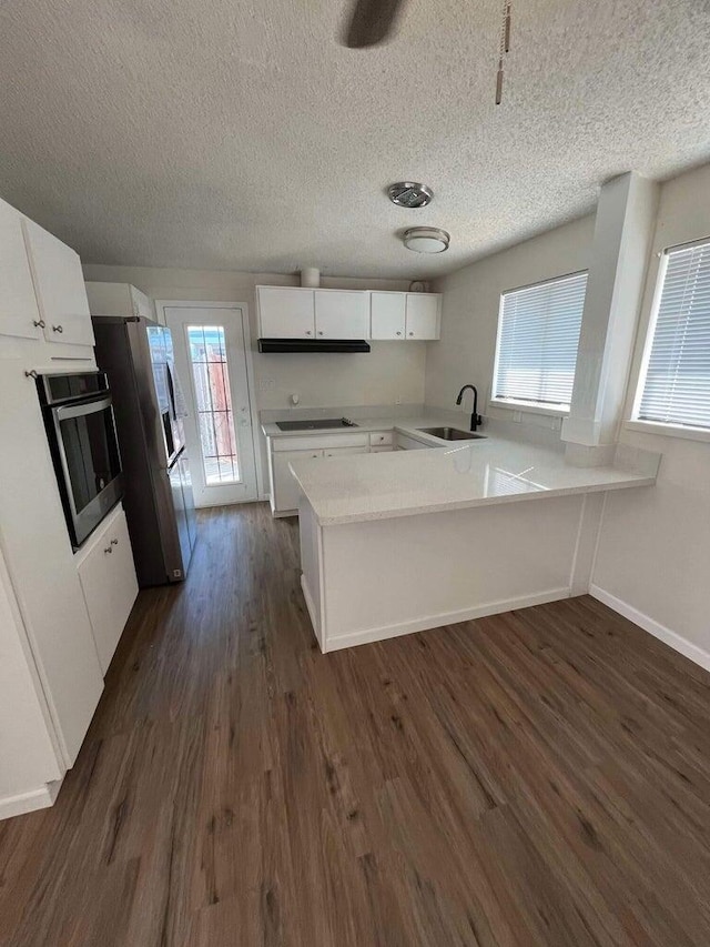 kitchen with sink, white cabinetry, stainless steel appliances, dark hardwood / wood-style flooring, and kitchen peninsula