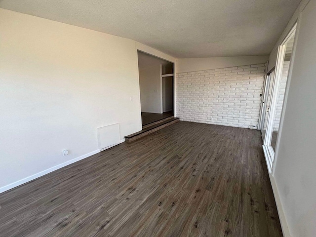 unfurnished bedroom with dark hardwood / wood-style floors, a textured ceiling, and brick wall