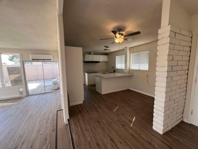 kitchen with sink, an AC wall unit, dark hardwood / wood-style flooring, kitchen peninsula, and white cabinets