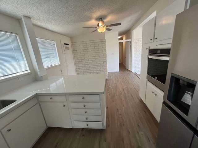 kitchen with dark wood-type flooring, stainless steel oven, white cabinets, and a textured ceiling