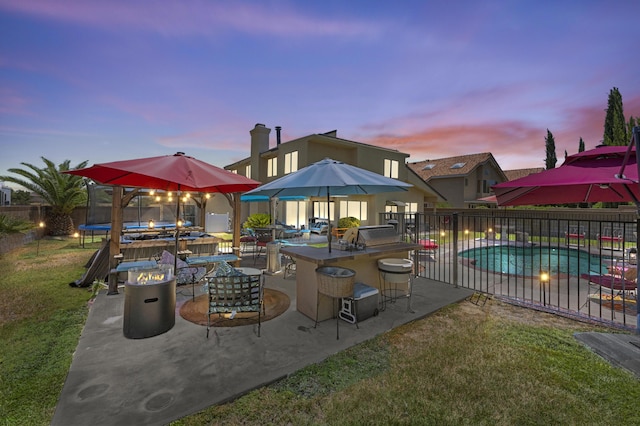 pool at dusk with a patio, an outdoor bar, a trampoline, and a lawn