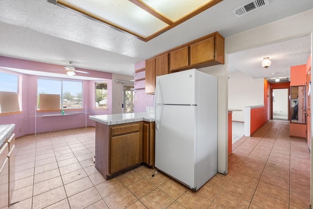40968 E 174th St, Lancaster, CA 93535 - kitchen featuring tile counters, a textured ceiling, brown cabinetry, freestanding refrigerator, and visible vents