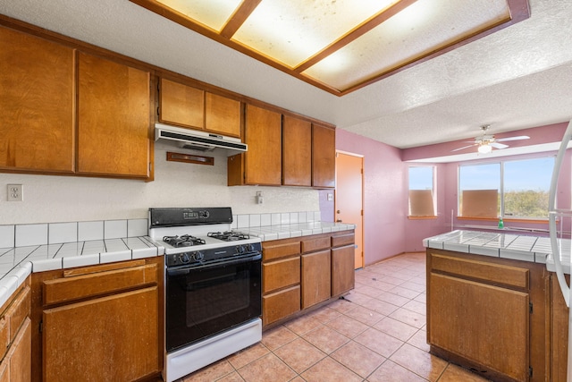 40968 E 174th St, Lancaster, CA 93535 - kitchen with gas stove, tile counters, brown cabinetry, and under cabinet range hood