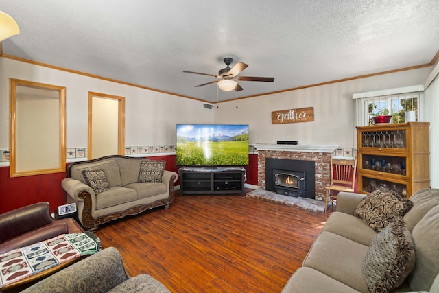 living room featuring ornamental molding, a textured ceiling, ceiling fan, hardwood / wood-style floors, and a wood stove