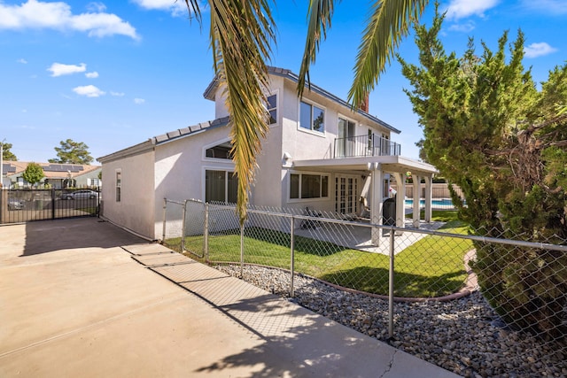 rear view of house featuring a yard, a patio area, a balcony, and a fenced in pool