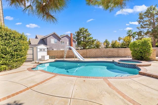 view of swimming pool with an in ground hot tub, a diving board, a water slide, a patio, and a storage unit