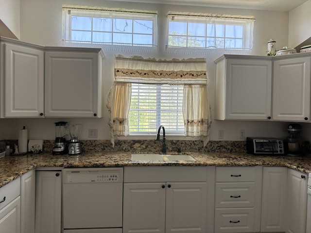 kitchen featuring dishwasher, dark stone countertops, white cabinetry, and sink