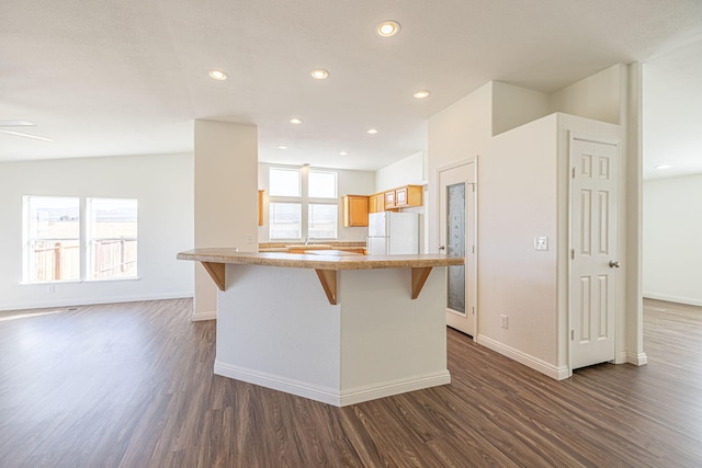 kitchen featuring white refrigerator, dark hardwood / wood-style flooring, a wealth of natural light, and a kitchen breakfast bar