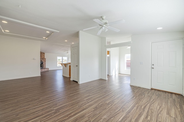 unfurnished living room featuring dark wood-type flooring, ceiling fan, lofted ceiling, and a stone fireplace