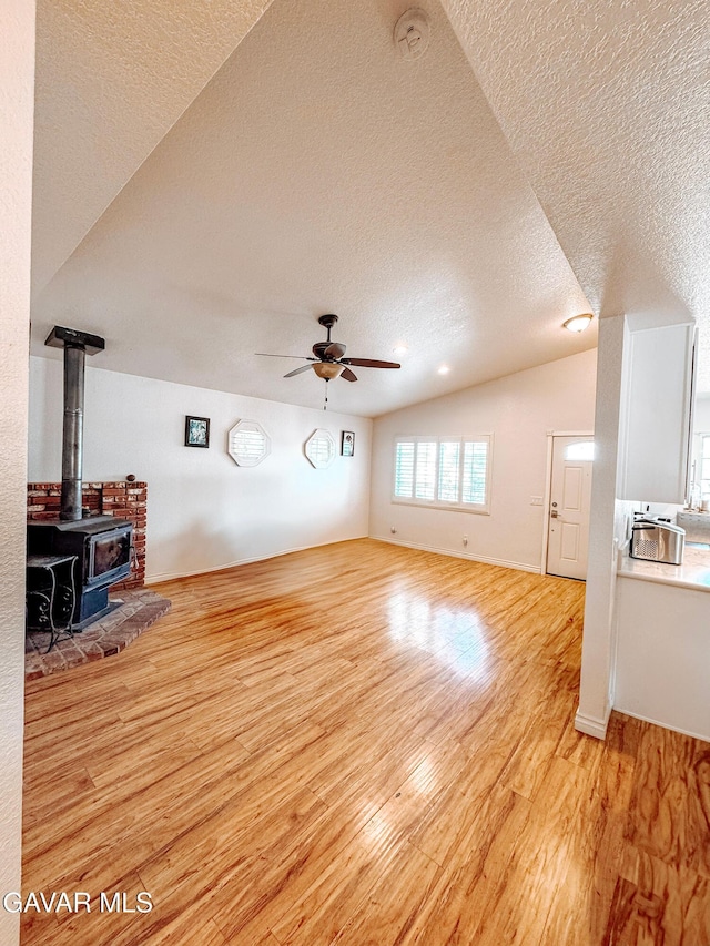 2895 59th St, Rosamond, CA 93560 - unfurnished living room with a textured ceiling, light wood-style flooring, ceiling fan, vaulted ceiling, and a wood stove