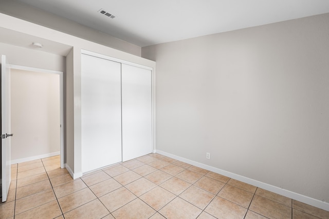 unfurnished bedroom with baseboards, visible vents, light tile patterned flooring, and a closet