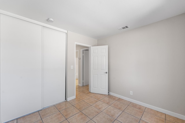 unfurnished bedroom featuring light tile patterned floors, visible vents, baseboards, and a closet