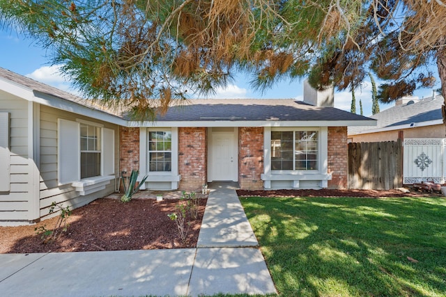 ranch-style home featuring a chimney, brick siding, fence, and a front lawn