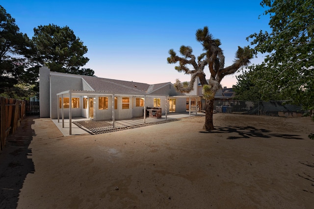 back of property at dusk featuring fence, a chimney, stucco siding, and a patio area