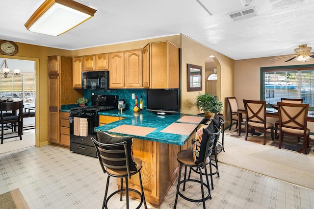 kitchen with black appliances, ceiling fan with notable chandelier, and a breakfast bar area